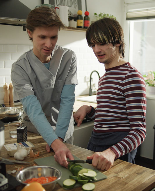 Care taker assisting young person in need with chopping vegetables