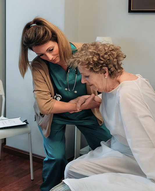Care taker assisting a woman sitting in bed to stand up