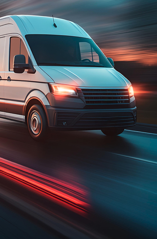 White delivery van driving fast on a road at dusk with motion blur.