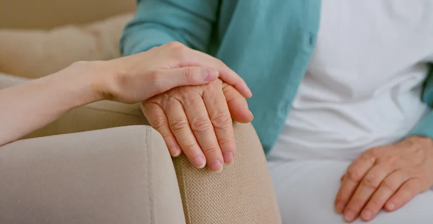 care giver holds older persons's hand