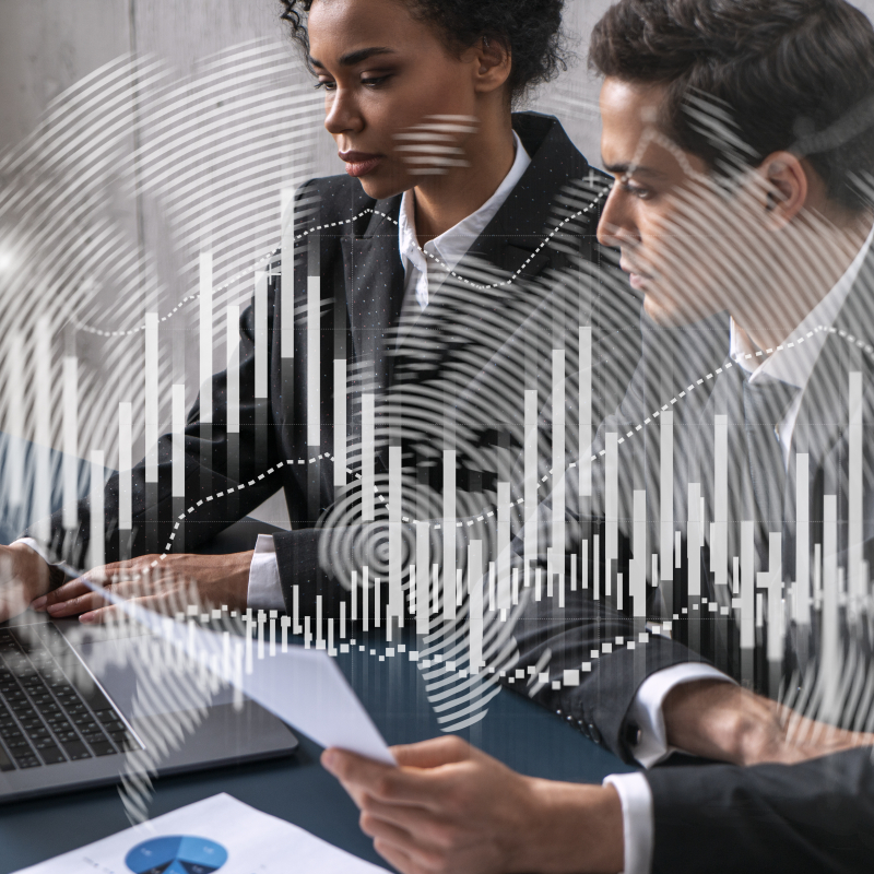 Two professionals working together at a desk, reviewing documents on a laptop, with abstract data charts and digital graphics overlaid, symbolising analysis, reporting and data-driven decision-making.